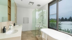 Ett modernt badrum med två tvättställ, en duschkabin med glasväggar och ett stort fönster med utsikt över stadsbilden.
