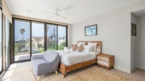 A bedroom with a large sliding glass door, a bed with a wooden headboard, a grey armchair, and a ceiling fan. - Clifftop Luxury With Pool ~ Ultimate outdoor experience with a private pool (Kiama)