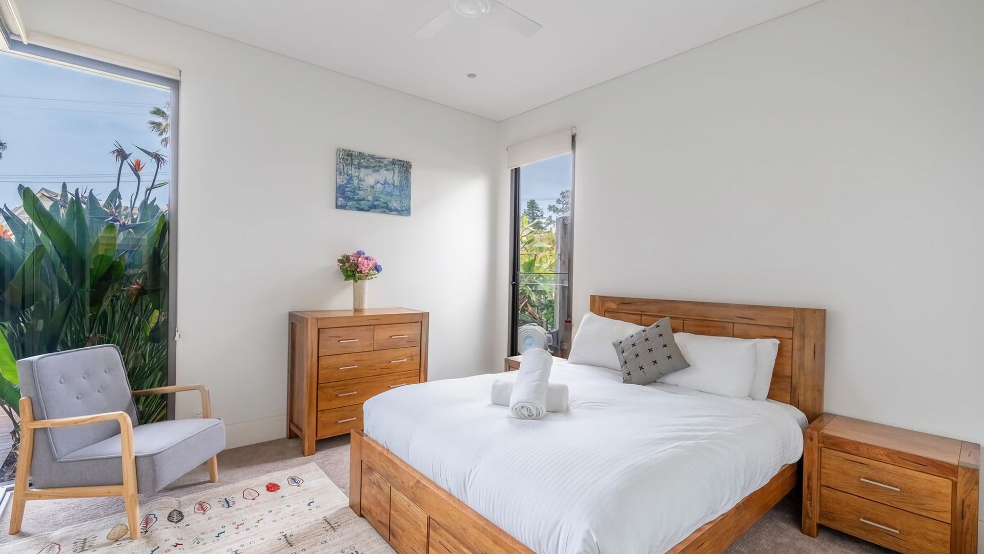 A bedroom with a wooden bed, a nightstand, a dresser, a chair, and a window with a view of greenery.