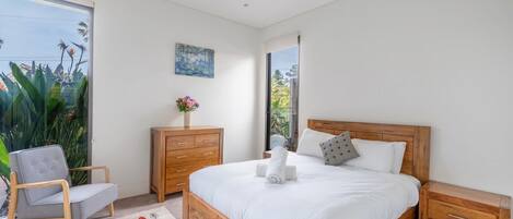 A bedroom with a wooden bed, a nightstand, a dresser, a chair, and a window with a view of greenery.