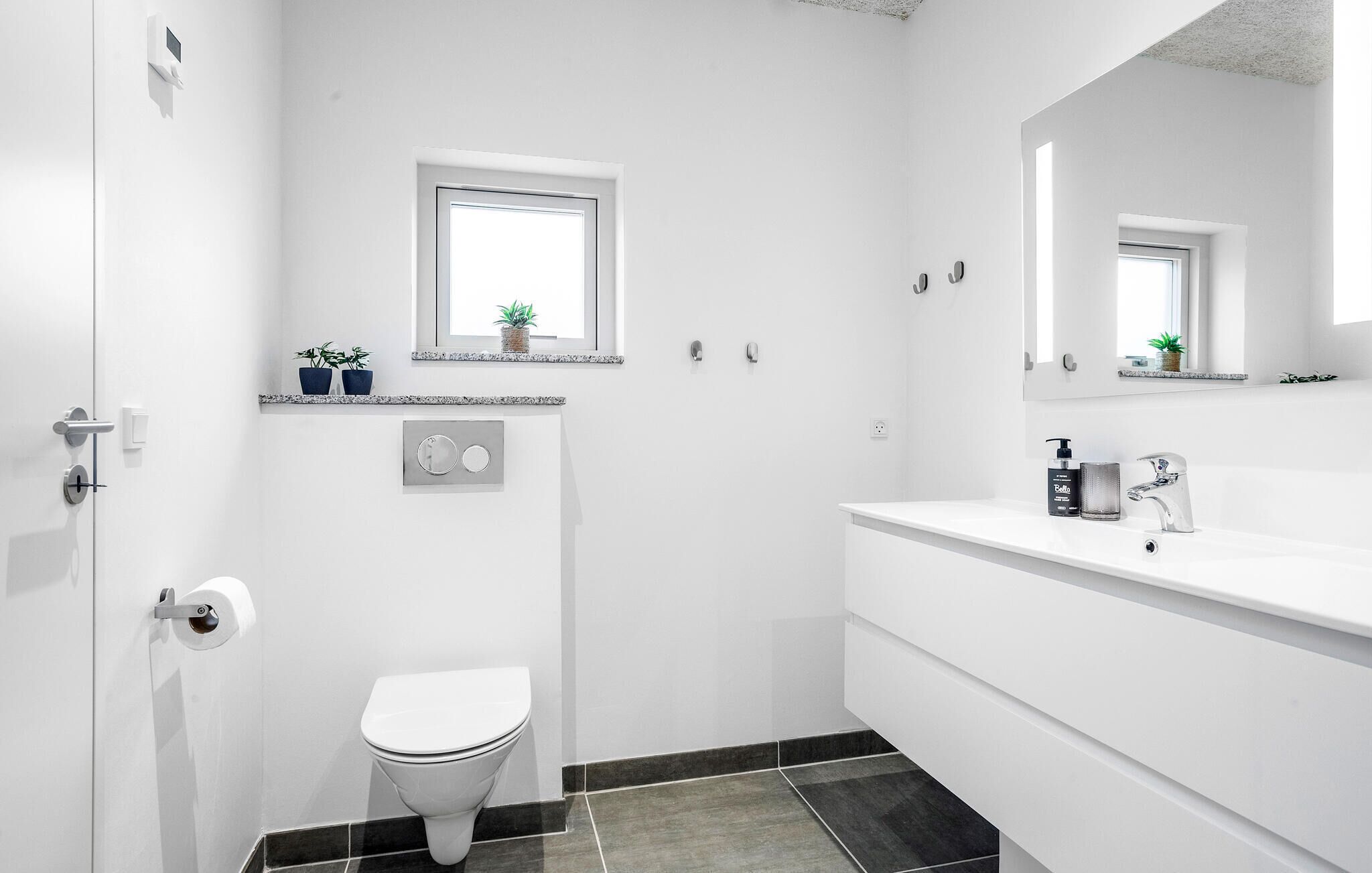 A modern bathroom with a toilet, sink, and a small window above the toilet.