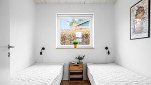 A small, clean room with two single beds, a window with a view of trees and a building, a small wooden nightstand with a plant, and a framed picture on the wall. - 4 bedroom awesome home in Slagelse (Slagelse)