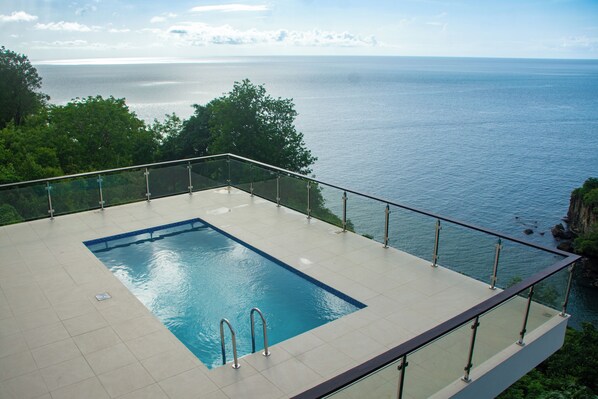 Piscina infinita en la azotea con barandillas de vidrio, con vistas a la costa.