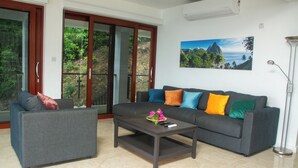Una sala de estar con un sofá gris, un sillón gris más pequeño, una mesa de centro y un cuadro de un paisaje montañoso.