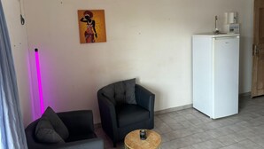 Un piccolo angolo living con un divano, una poltrona, un tavolino, un frigorifero e un'opera d'arte appesa al muro.