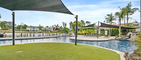 A swimming pool with a surrounding deck, lounge chairs, and a shaded area.