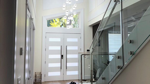 A modern interior with a staircase, glass railings, and a chandelier. - Luxury Spacious House (Surrey)
