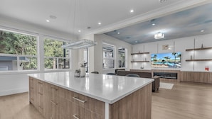 A spacious kitchen with a large island, wooden cabinets, and a modern chandelier. - Luxury Spacious House (Surrey)
