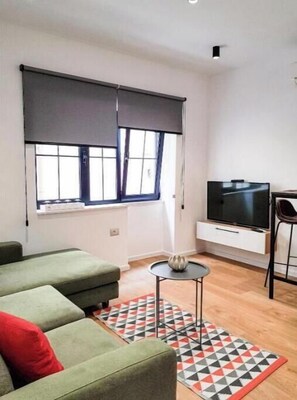 Relax in this stylish living room with a sofa, coffee table, and TV, set against a beautiful rug and large windows.