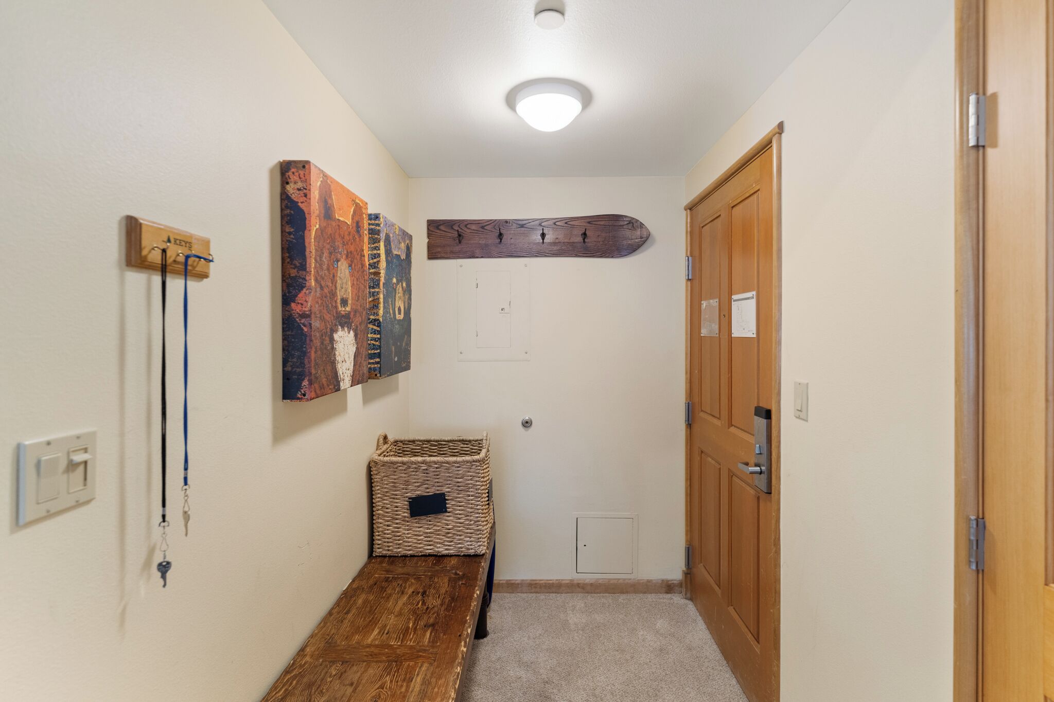 A hallway with a wooden bench, a wall-mounted coat rack, a wooden door, and a wall-mounted artwork.