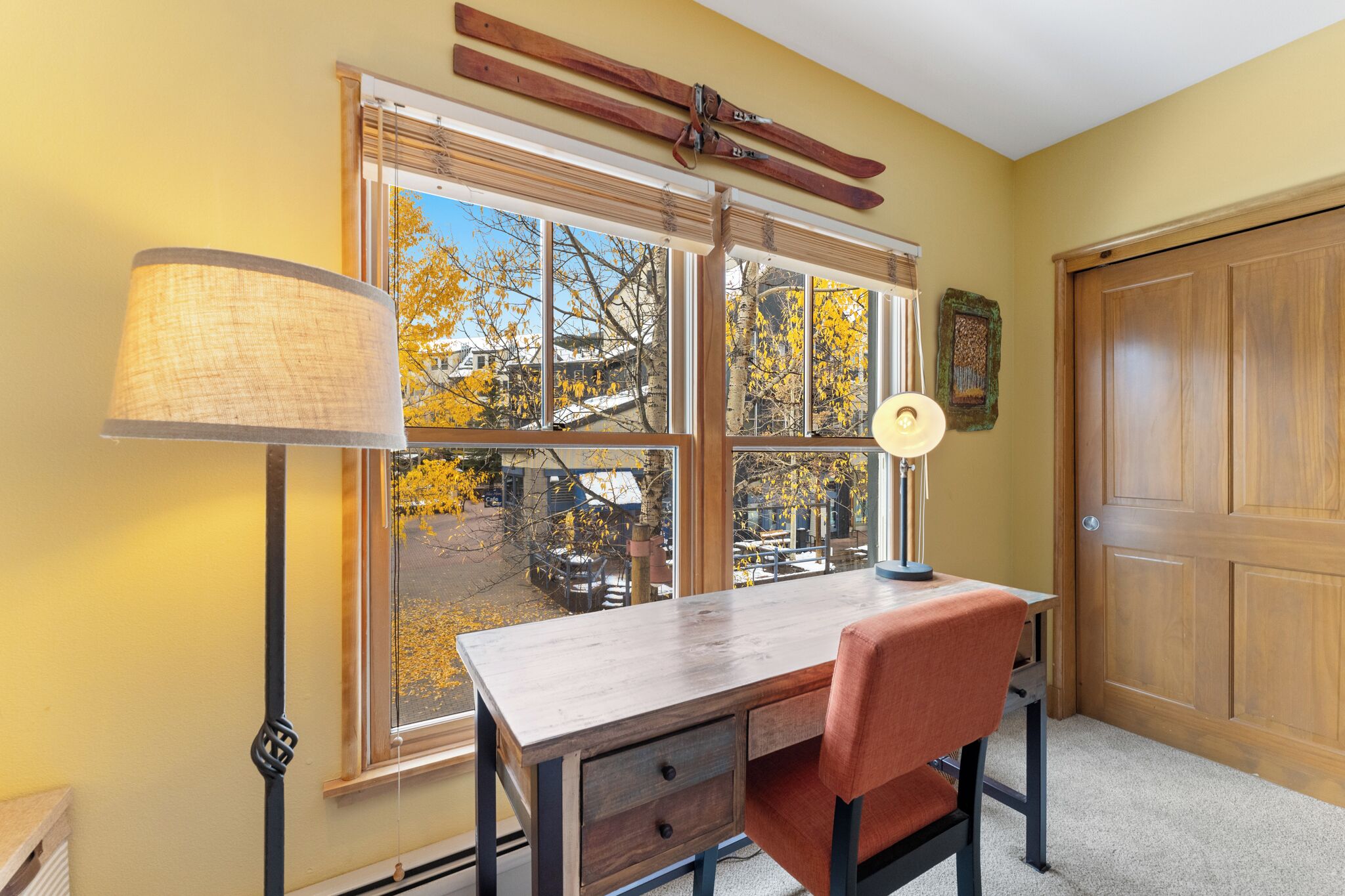 A room with a desk, chair, lamp, window, and door.