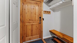 Una puerta de madera con un tirador de metal, un estante con ganchos y un banco.