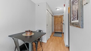 Un pasillo estrecho con una mesa y sillas de comedor, una puerta de madera y un cuadro en la pared.