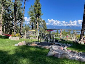 A well-maintained garden with a wooden deck, a metal bench, and a view of mountains.