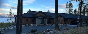 A modern wooden house with a stone entrance, a driveway, and a view of a lake.