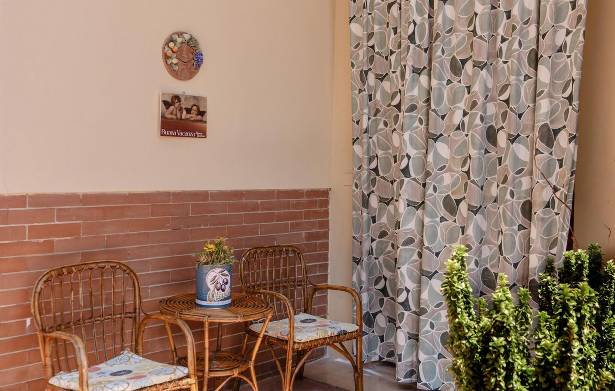 A corner with a brick wall, a round table with chairs, a decorative plate, a framed picture, and a patterned curtain.