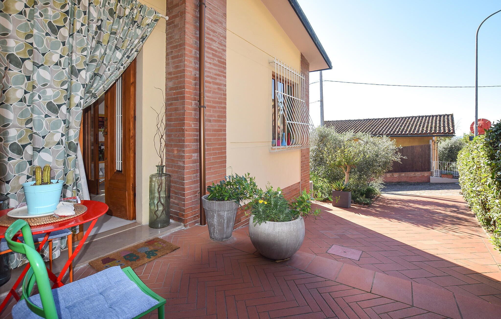 A patio with a brick floor, a small table, a chair, and potted plants.