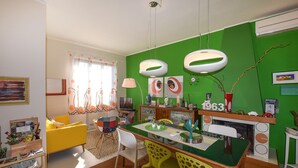 Ein helles Wohnzimmer mit grüner Akzentwand, einem gelben Sofa und einem Essbereich mit grünem Tisch und gelben Stühlen.