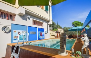 Zona de piscina con silla de salvavidas, una pequeña estatua y una fuente decorativa.