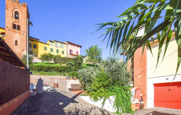 Una stretta strada acciottolata fiancheggiata da edifici, con un campanile e un cancello rosso.