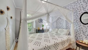 A bedroom with a canopy bed, a macrame wall hanging, a feather-patterned wallpaper, and a round mirror. - Chic and Comfy apartment centralized in Rochester (Rochester)