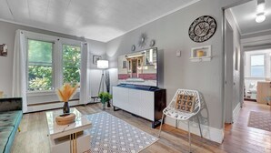 A modern living room with a large window, a white sofa, a coffee table, a TV, and a decorative clock on the wall. - Chic and Comfy apartment centralized in Rochester (Rochester)