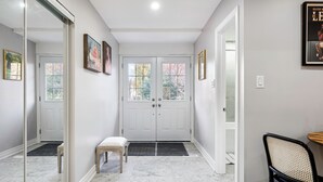 Un pasillo con una puerta blanca, un banco y una silla.