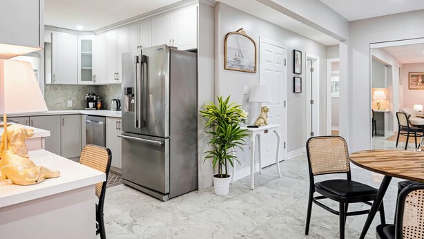 Una cocina moderna con armarios blancos, electrodomésticos de acero inoxidable y un comedor con mesa y sillas de madera.