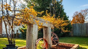 Un jardín con un arco de madera, una rueda de metal y un comedero para pájaros.