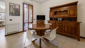 Un comedor con una mesa redonda, sillas blancas, un armario de madera, un televisor y un radiador.
