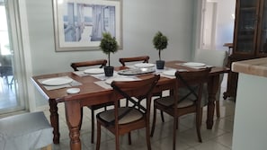 Un comedor con una mesa de madera dispuesta para cuatro personas, rodeada de sillas. Hay dos plantas en macetas sobre la mesa y un cuadro enmarcado en la pared de arriba.