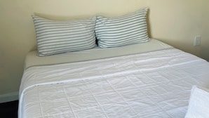 Una cama bien hecha con una colcha blanca acolchada y dos almohadas a rayas.