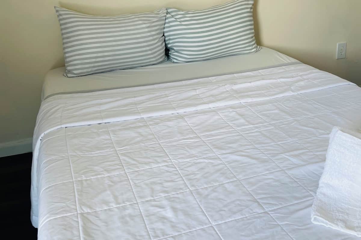 A neatly made bed with a white quilted bedspread and two striped pillows.
