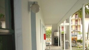 Un espacio exterior techado con sillas de plástico blanco, piso de concreto y vista a un edificio residencial al fondo.
