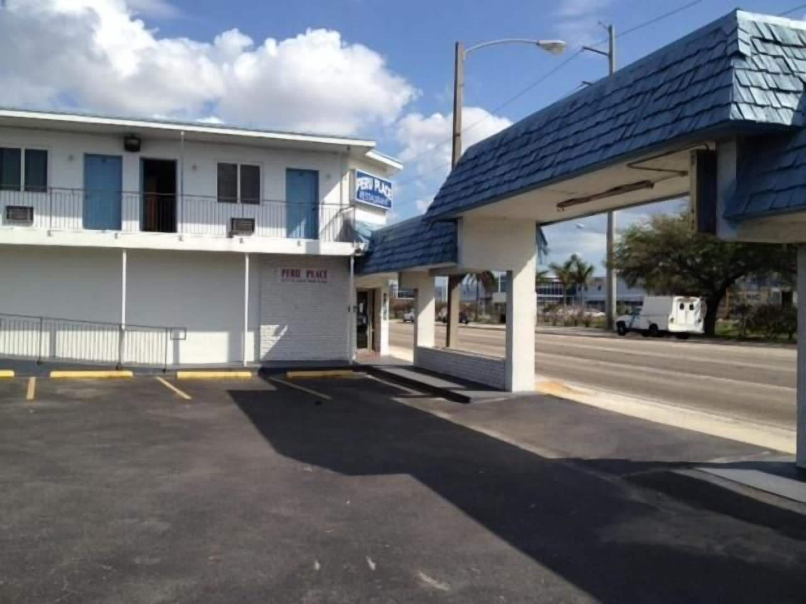 A motel with a covered parking area and a building with a blue awning.