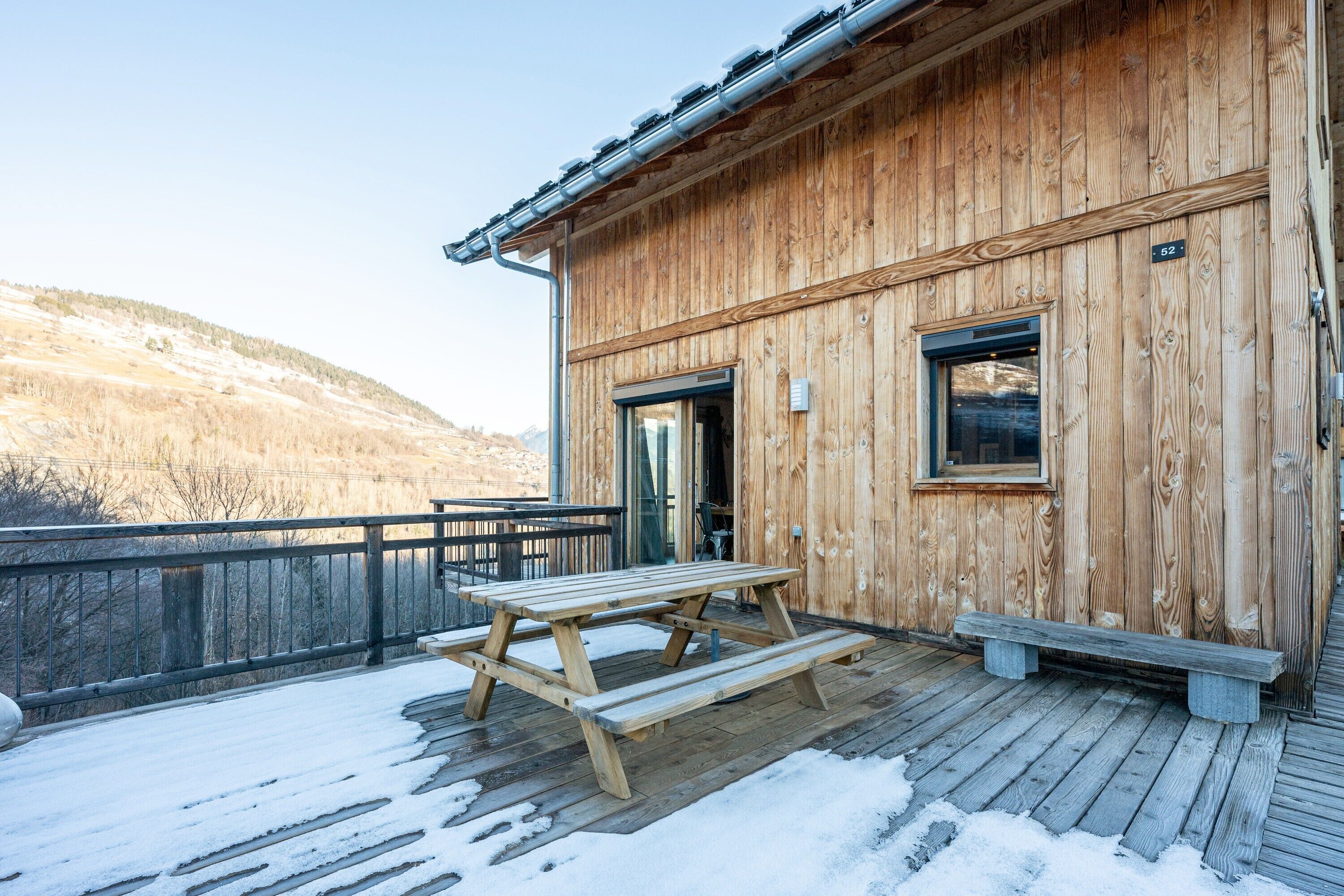 Une cabane en bois avec une table de pique-nique et des bancs sur une terrasse enneigée.
