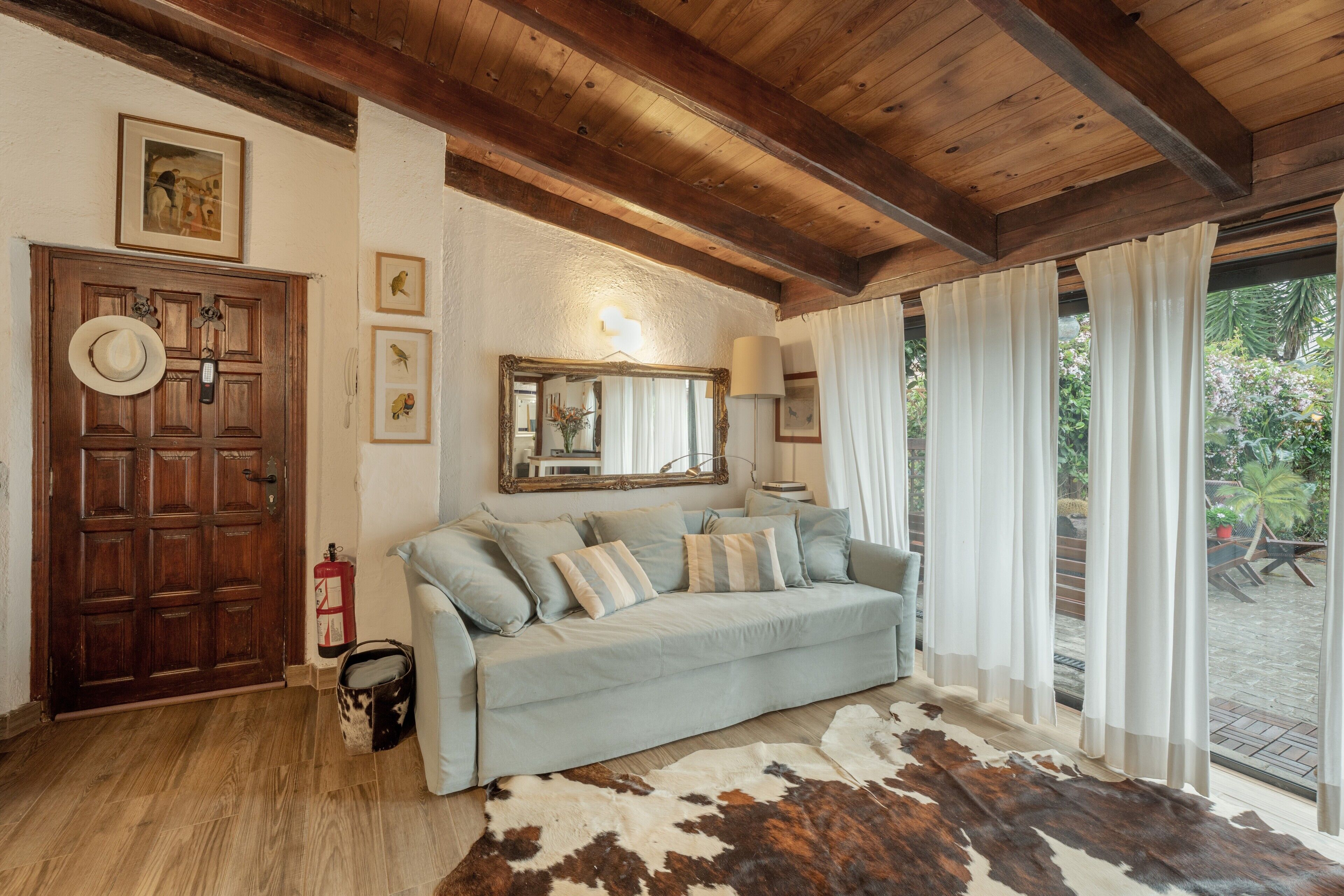 A room with a wooden ceiling, a light blue sofa, a cowhide rug, a wooden door, and a fire extinguisher.