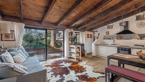 Uma sala ampla com sofá, mesa de jantar, cozinha com fogão e uma grande janela com vista para o verde.