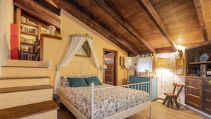 Quarto com cama, escada de madeira, estantes e um pequeno armário.