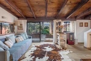Un salón con techo de madera, un sofá, un tapete de piel de vaca, un refrigerador y vistas al exterior.