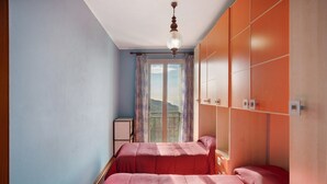 Un dormitorio con dos camas, una ventana con cortinas, un armario y una lámpara en el techo.