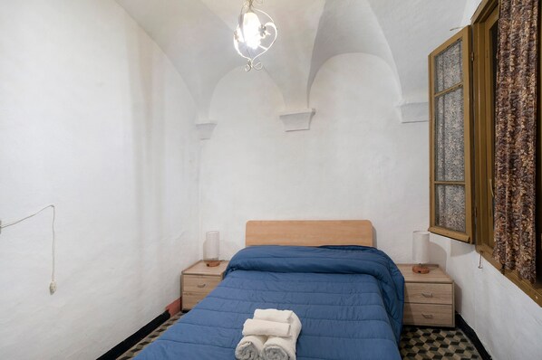 Una habitación con cama, mesita de noche, lámpara y ventana con cortinas.