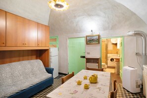 A compact room with a sofa, a table with kitchenware, a washing machine, and a small refrigerator.
