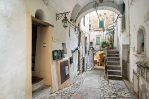 Un estrecho callejón empedrado con edificios de piedra, un arco y una escalera que sube a un nivel superior.