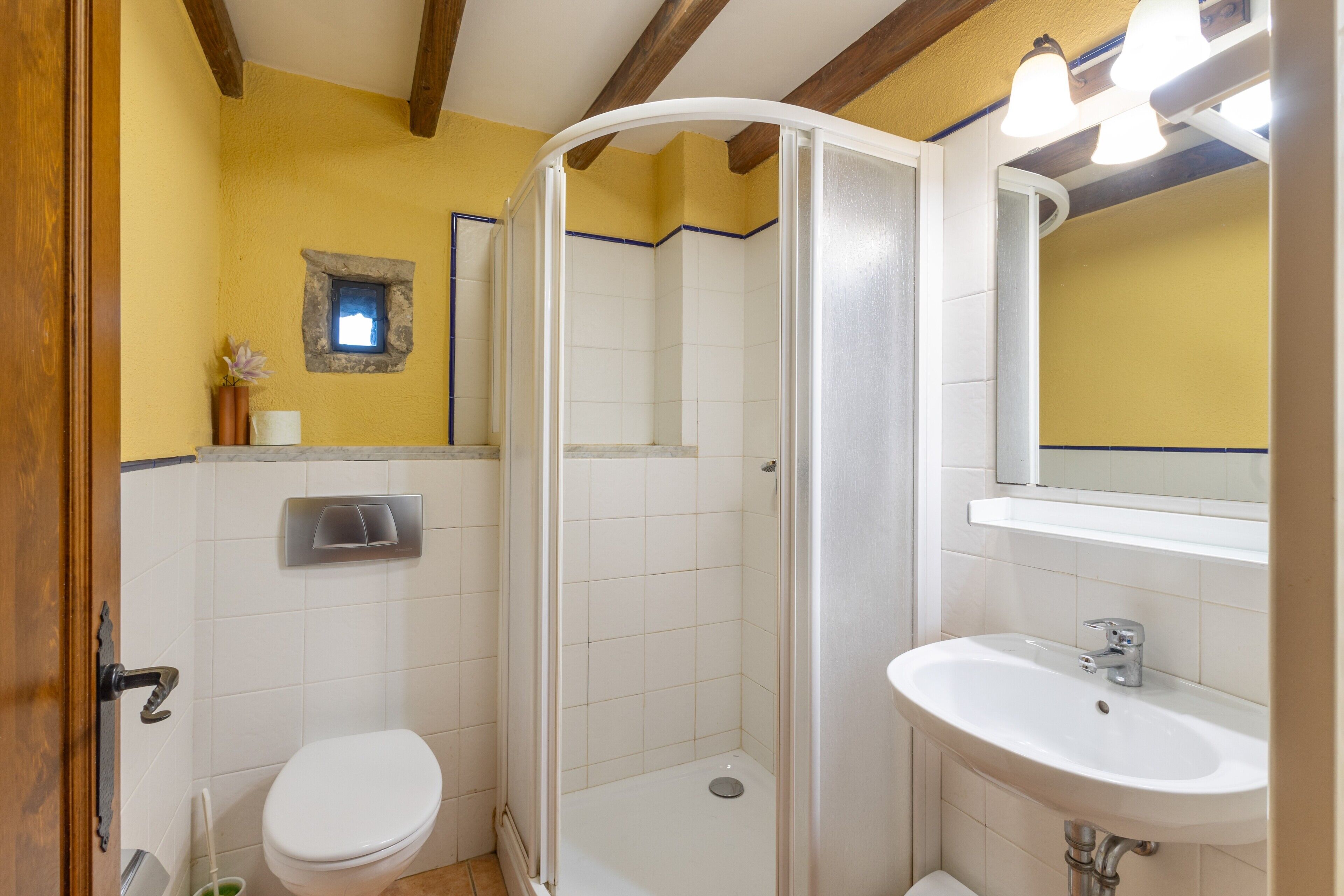 Un baño con inodoro, ducha, lavabo y un pequeño ventanal.