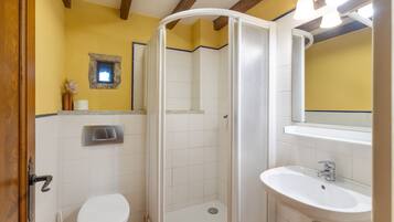 Un baño con inodoro, ducha, lavabo y un pequeño ventanal.