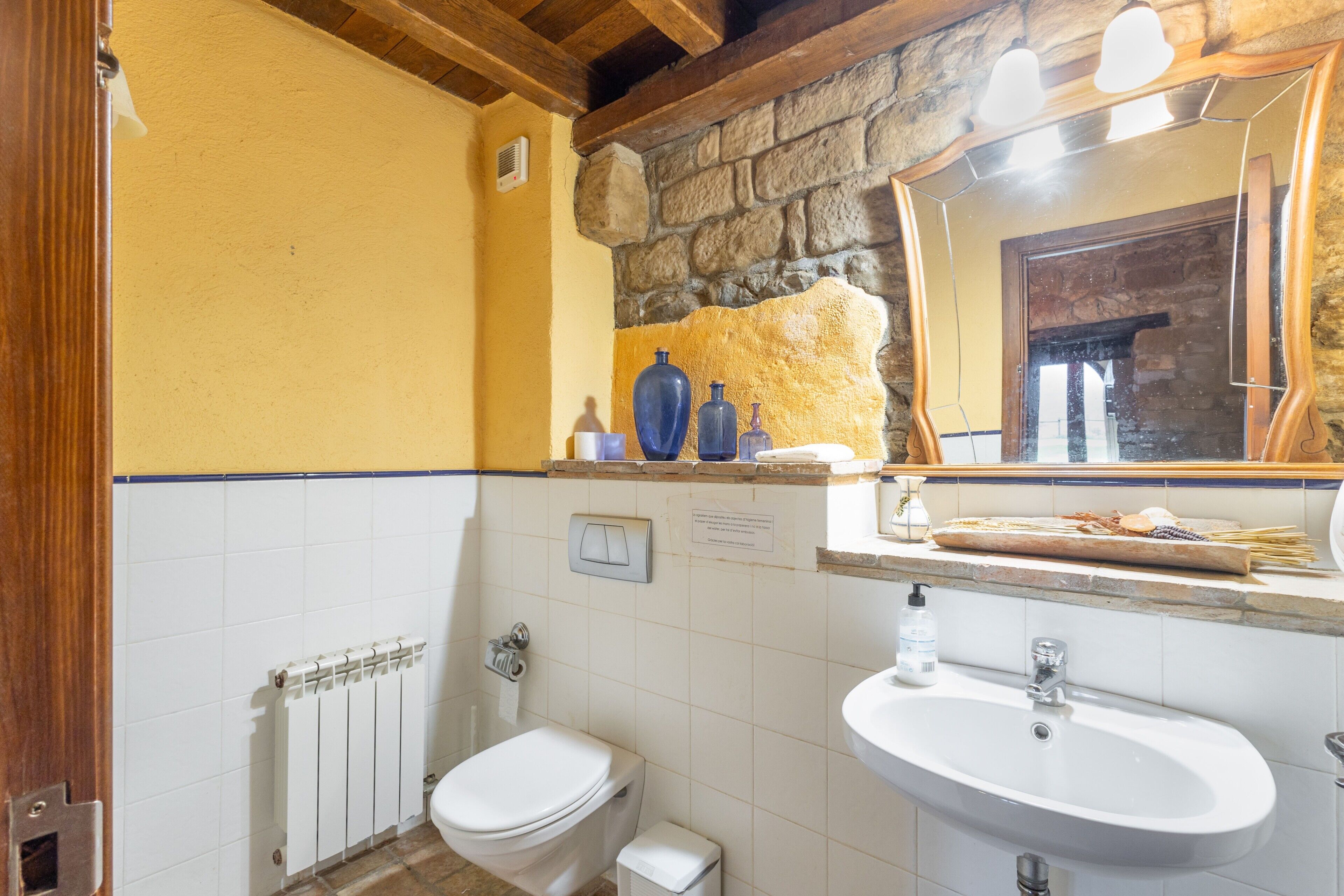 Een badkamer met een wit toilet, een wastafel, een spiegel en een stenen muur.