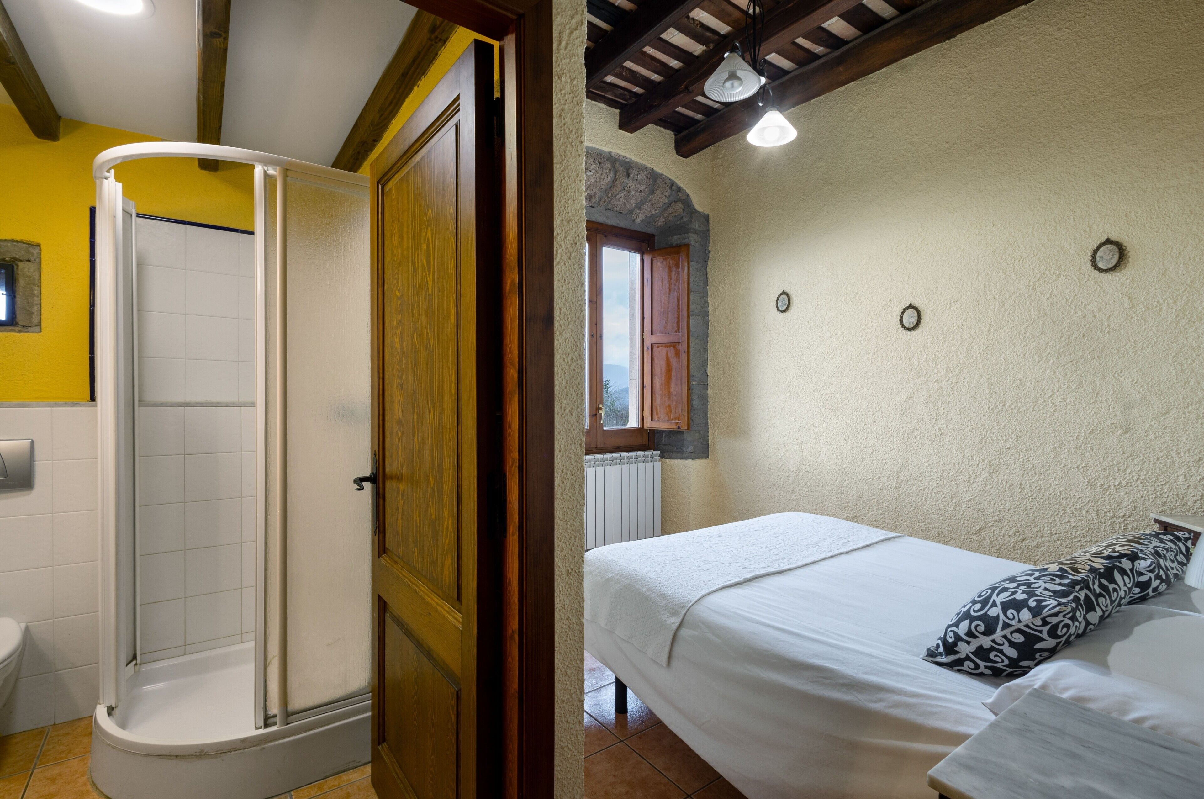Ein Badezimmer mit Dusche, Toilette und einem Bett mit einem gemusterten Kopfkissen.