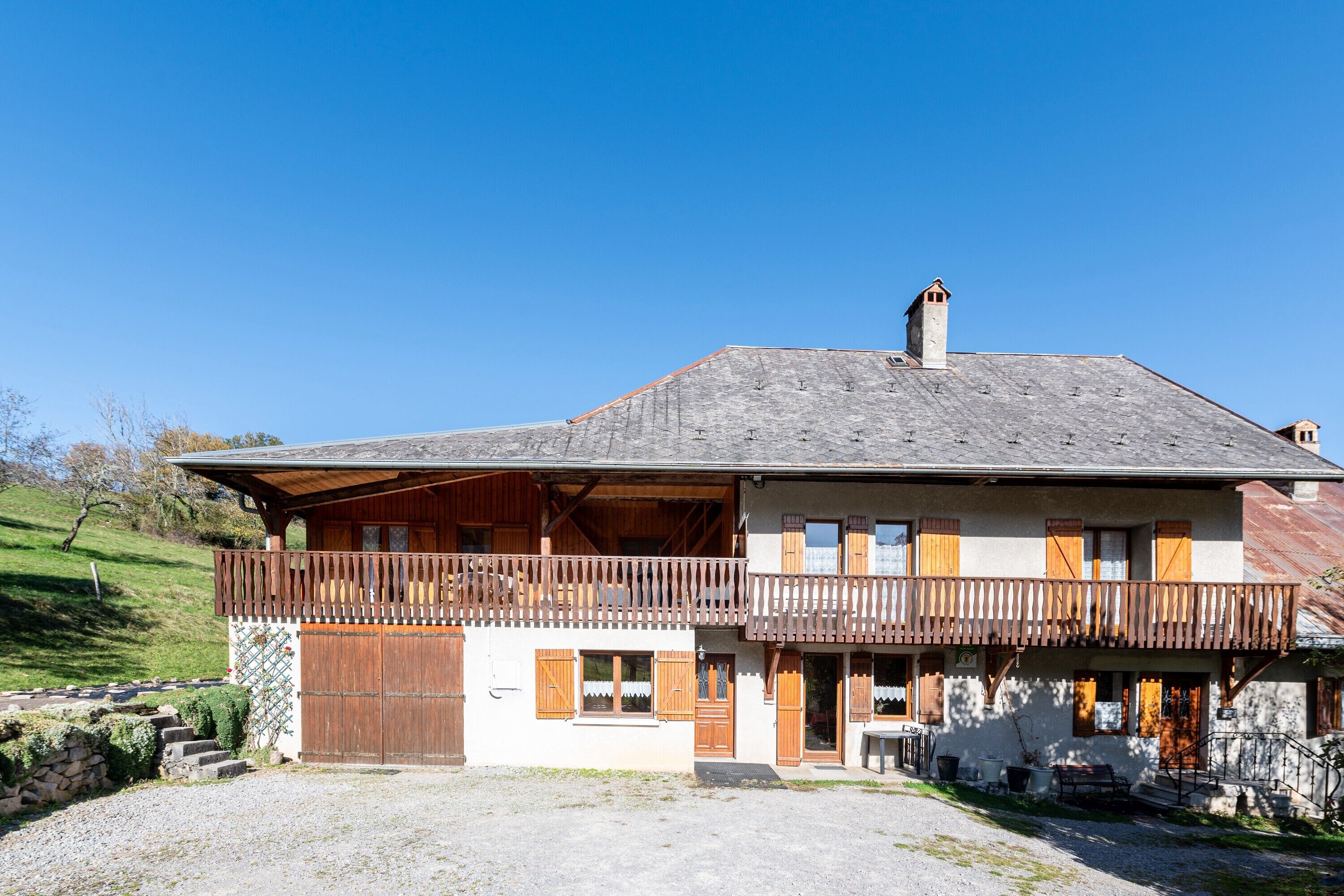 A two-story building with a balcony, a stone wall, and a gravel driveway.