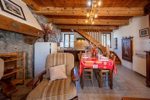 A rustic interior with a wooden ceiling, stone walls, a dining table set for four, and a sofa with a cushion. - Cottage 'La Belle Étoile' with Mountain View and Shared Garden (Faverges-Seythenex)